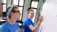 Two female students standing at a dry erase board working together on homework.